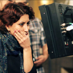 An Image Of Mahsa. She Has One Hand On Her Chin As She Is Looking At A Screen On Set.