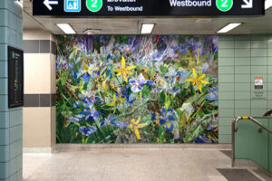 An interior shot of Chester subway Station. On a teal tile wall is a vibrant mural featuring yellow and blue flowers on a green grassy background.