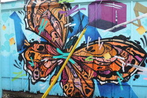 A picture of a mural featuring a bright orange butterfly on a light blue background. The line work is expressive and bold.