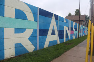 A picture of a wall painted in blocky blue tiles. In large white block letters reads, "Transitions".