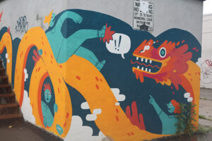 A picture of a mural featuring an orange and yellow Eastern dragon. One person, painted in blue, sits on top of the dragon's back, another person points towards him, seemingly shocked at what they're witnessing. A third figure peers through the loops of the dragon's body.