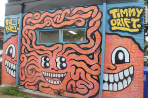 A picture of a mural featuring an orange creature with many noodle-like arms, four eyes and a grinning mouth.