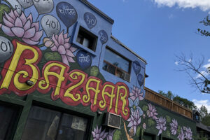 A picture of a colourful mural on the side of a building. In bold yellow letters reads, "Bazaar". Pink lotus flowers are painted throughout the mural.