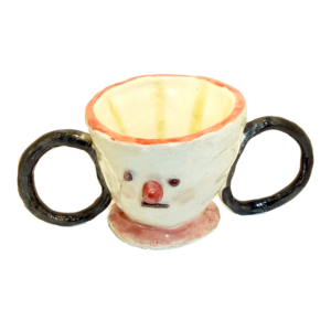 A Picture Of A Ceramic Tea Cup. It Has A Small Face With A Small Protruding Red Nose, And Two Black Handles On Either Side.