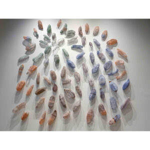 A Photo Of An Art Installation On A Gallery Wall. The Installation Features Three-dimensional Multicoloured Grains Constructed From Wrapping Wire. They Are Affixed To The Wall.
