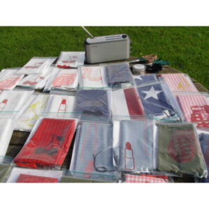 An Outdoor Shot Of A Bunch Of Printed Textiles In Ziploc Bags On A Table. In The Top Of The Image Is A Radio And Crafting Supplies, Such As Scissors.