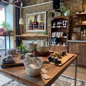 An Interior Shot Of The Riverdale Hub Cafe Featuring Display Shelves Carrying Homemade Goods. There Is An Exposed Brick Wall And The Tables Are Made Of Stained Wood.