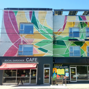 An exterior shot of the Riverdale Hub and the Hub Gallery. The exterior of the brick building is painted in a vibrant geometric pattern.