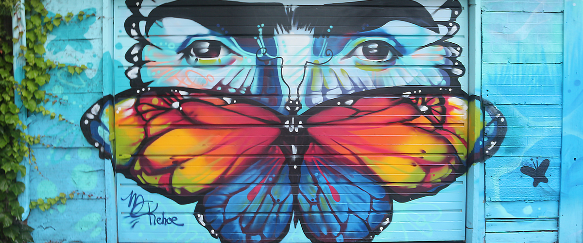 A photo of a mural featuring a butterfly and the upper half of a face on a vibrant blue background.