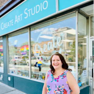 A photo of the Create Art Studio storefront. The owner, a woman in a floral top, stands out front, smiling.