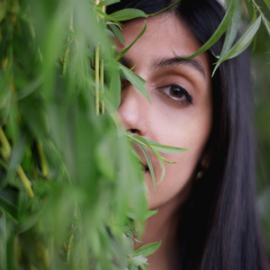 A headshot of Zen Alladina, a South Asian woman. Willow leaves hand and obscures half her face.