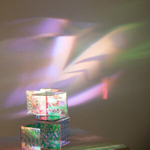 Colourful Paper Cubes Cast Prismatic Light Up Against A White Wall.