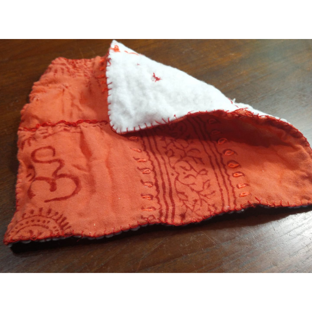 A square of orange fabric with one corner turned to show the backing, hand-tacked down with a blanket stitch around the edge.